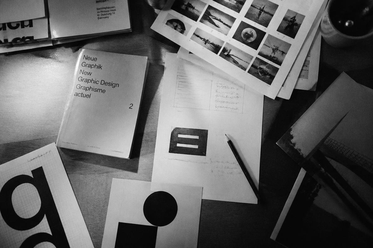 Mesa de trabalho com provas impressas, livro de design gráfico e anotações a lápis